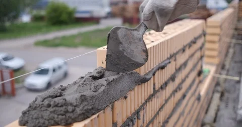 Builder in gloves puts brick in mortar, taps on it, shallow depth of field Stock Footage 116793723