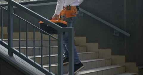 Builder goes up stairs with toolbox and helmet in hands Video stock 258738459