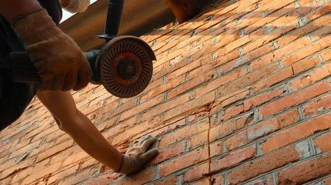 Builder with a grinder and a stone cutting disc stands by a brick wall Stock Photos