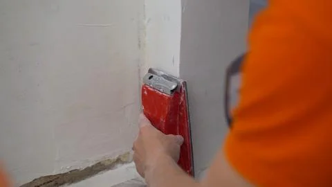 The builder grinds the wall from irregularities after applying putty. Sanding Stock Photos