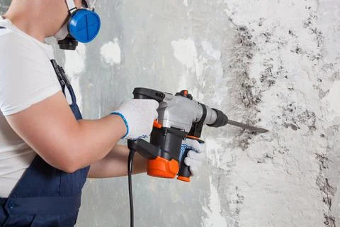 The builder with hammer drill perforator equipment making hole in wall at con Stock Photos