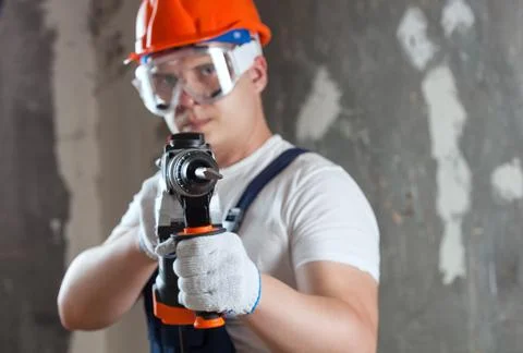 The builder with hammer drill perforator equipment making hole in wall at con Stock Photos
