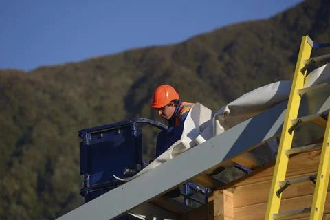 A builder hammers down building paper as the team puts the roof on a large Fotos de archivo