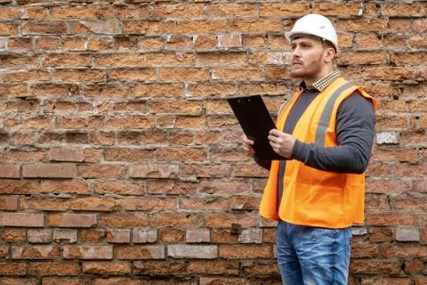 Builder in a hard hat on a brick wall background. Stock Photos