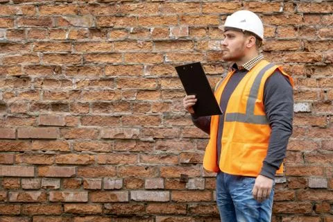 Builder in a hard hat on a brick wall background. Stock Photos