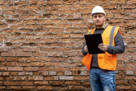 Builder in a hard hat on a brick wall background. Stock Photos