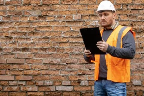 Builder in a hard hat on a brick wall background. Stock Photos