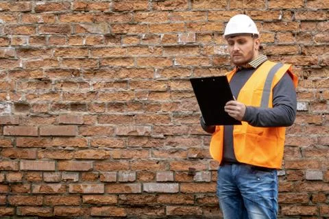 Builder in a hard hat on a brick wall background. Stock Photos