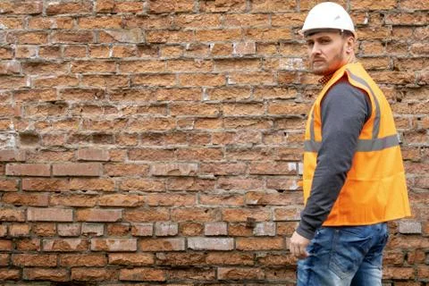 Builder in a hard hat on a brick wall background. Stock Photos