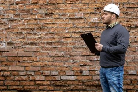 Builder in a hard hat on a brick wall background. Stock Photos