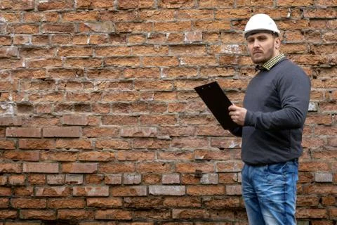 Builder in a hard hat on a brick wall background. Stock Photos