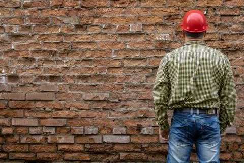 Builder in a hard hat on a brick wall background. Stock Photos