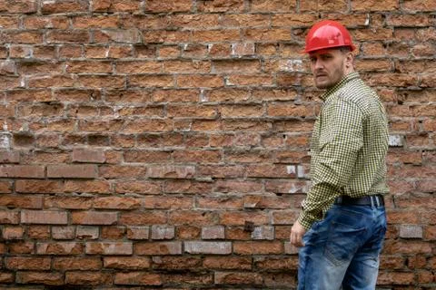 Builder in a hard hat on a brick wall background. Stock Photos