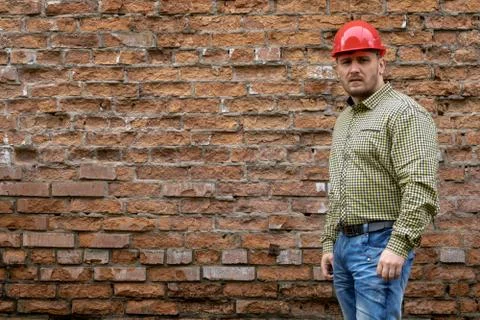 Builder in a hard hat on a brick wall background. Stock Photos