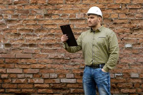 Builder in a hard hat on a brick wall background. Stock Photos