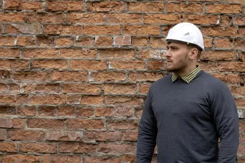 Builder in a hard hat on a brick wall background. Stock Photos