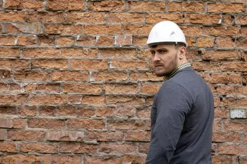 Builder in a hard hat on a brick wall background. Stock Photos