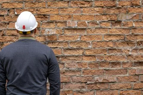 Builder in a hard hat on a brick wall background. Stock Photos