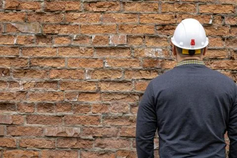 Builder in a hard hat on a brick wall background. Stock Photos