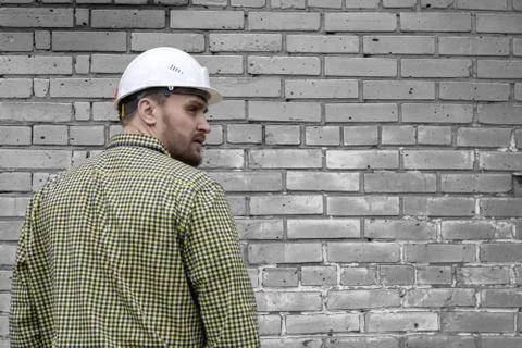 Builder in a hard hat on a brick wall background. Stock Photos