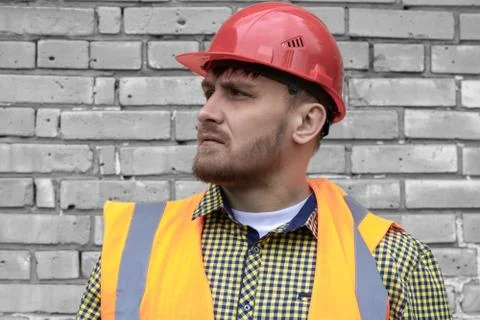 Builder in a hard hat on a brick wall background. Stock Photos