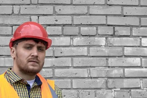 Builder in a hard hat on a brick wall background. Stock Photos