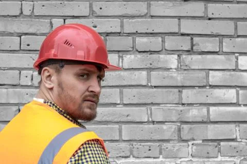 Builder in a hard hat on a brick wall background. Stock Photos