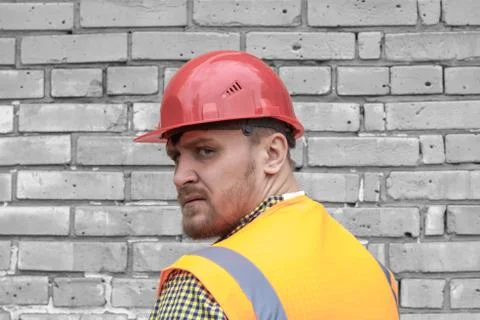 Builder in a hard hat on a brick wall background. Stock Photos