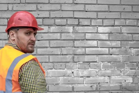 Builder in a hard hat on a brick wall background. Stock Photos