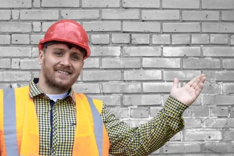 Builder in a hard hat on a brick wall background. Stock Photos