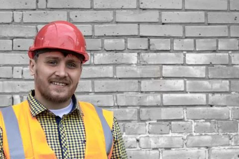 Builder in a hard hat on a brick wall background. Stock Photos