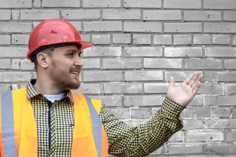 Builder in a hard hat on a brick wall background. Stock Photos