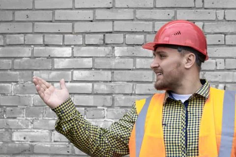 Builder in a hard hat on a brick wall background. Stock Photos