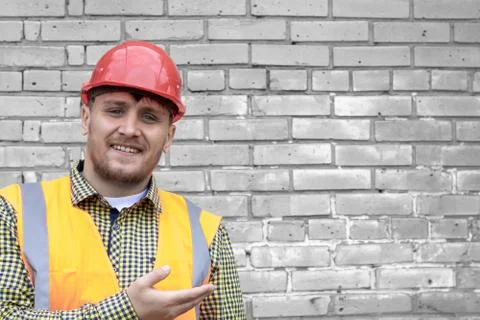 Builder in a hard hat on a brick wall background. Stock Photos