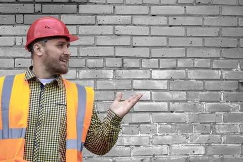 Builder in a hard hat on a brick wall background. Stock Photos
