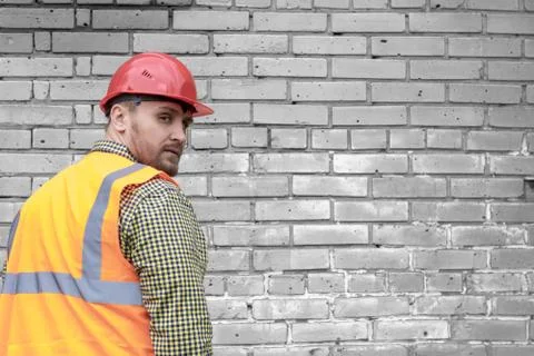 Builder in a hard hat on a brick wall background. Stock Photos