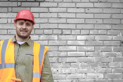 Builder in a hard hat on a brick wall background. Stock Photos