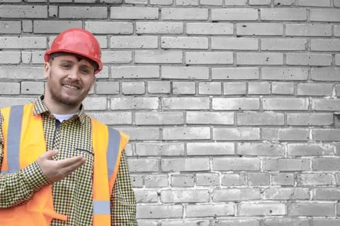 Builder in a hard hat on a brick wall background. Stock Photos