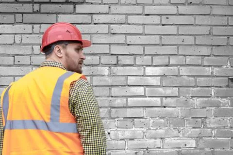 Builder in a hard hat on a brick wall background. Stock Photos