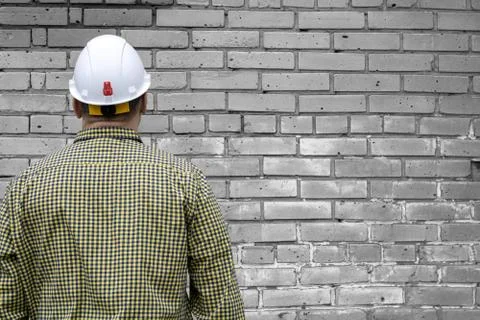 Builder in a hard hat on a brick wall background. Stock Photos