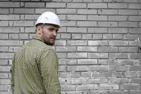 Builder in a hard hat on a brick wall background. Stock Photos