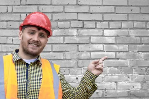 Builder in a hard hat on a brick wall background. Stock Photos