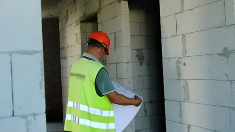 Builder in hard hat inspects floor plan before entering room 스톡 동영상 317609093