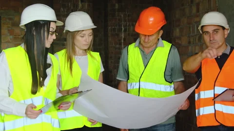 Builder in hard hat points at blueprint talking to colleagues Stock Footage 317612187