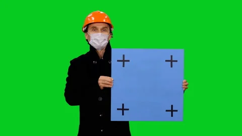 Builder in hardhat and mask something presenting and holding blue billboard Vídeo Stock 130836226