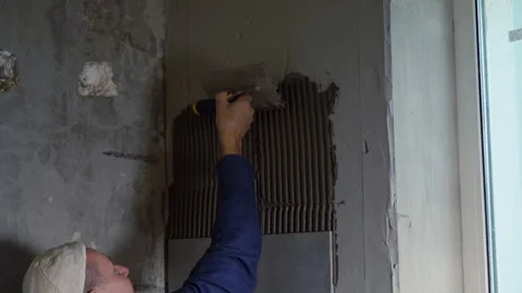 Builder in hardhat applying tile adhesive to wall Stock Footage 142106186