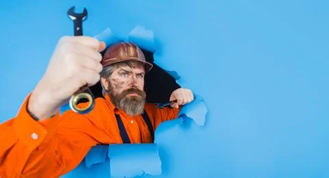 Builder in hardhat with wrench looking through paper hole. Bearded man with s Stock-Fotos