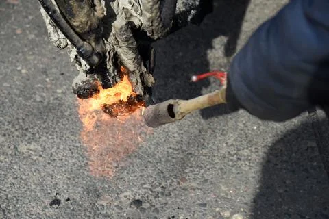 The builder heats the tool with fire, prepares to fill road holes with resin. Stock Photos