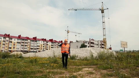 A builder in a helmet and vest is walking and talking on the phone. Stock Footage 129059948