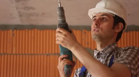 Builder in a helmet is drilling the ceiling. Construction work Video stock 61728235